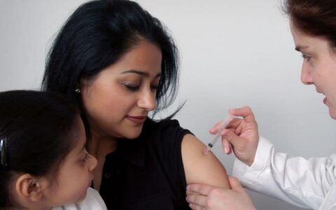 Refugee woman receives a vaccine with her daughter looking on
