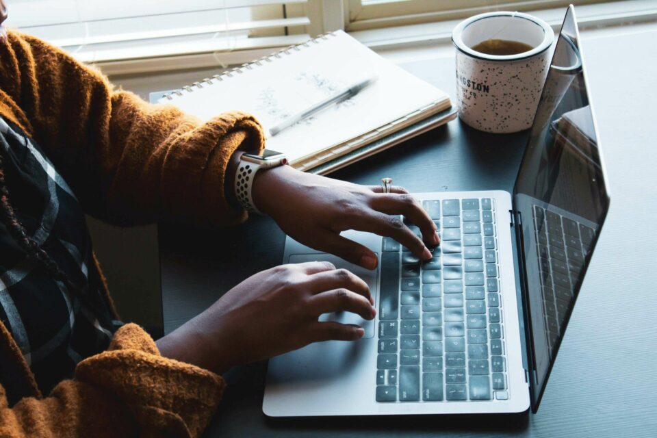 Woman sits at a laptop computer with a cup of tea and a book